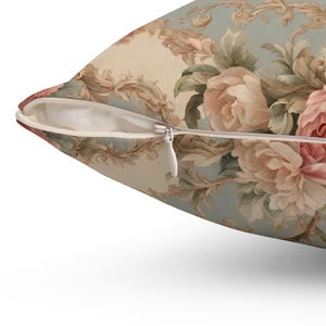 May include: Cushion with a floral pattern of pink and cream roses on a pale blue backdrop. The pillow has a concealed zip and a vintage style. The design includes ornate scrollwork.
