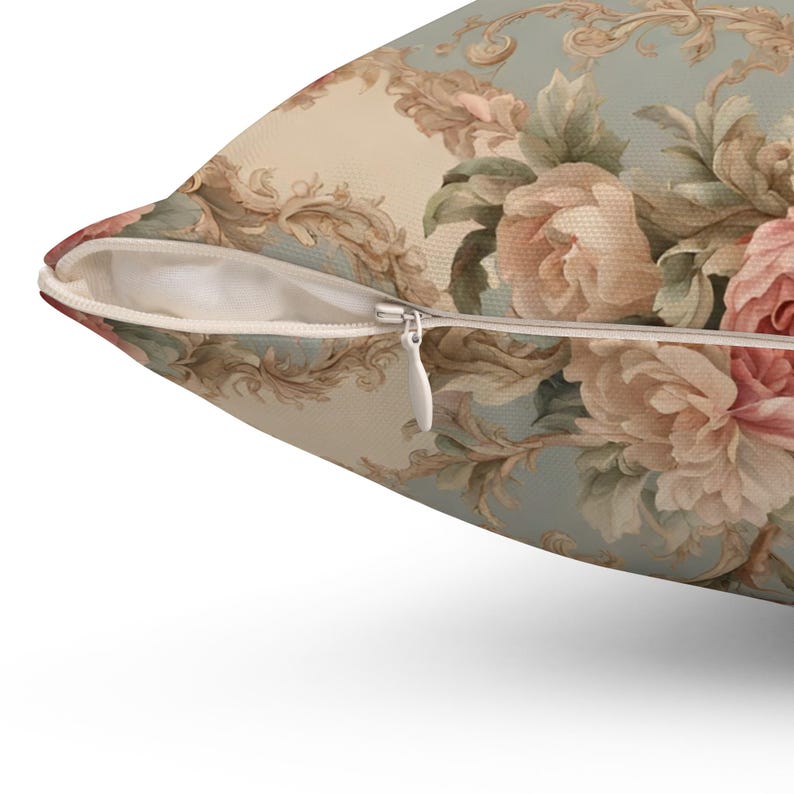 May include: Cushion with a floral pattern of pink and cream roses on a pale blue backdrop. The pillow has a concealed zip and a vintage style. The design includes ornate scrollwork.