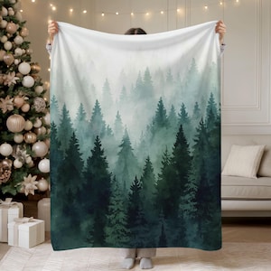 May include: A cozy blanket featuring a forest scene with tall evergreen trees in shades of green and teal, shrouded in a misty fog. The design creates a serene and natural aesthetic, perfect for home decor.