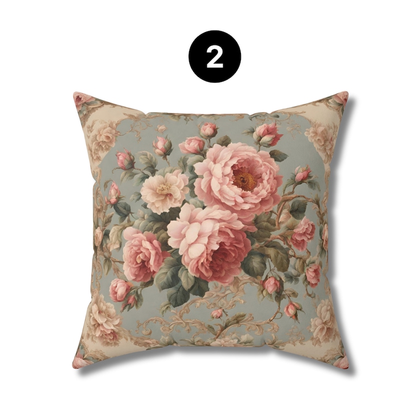 May include: Square cushion with a floral design. The cushion has a light blue background with a large bouquet of pink and cream-coloured roses. The edges have a decorative border. The number "2" is in a black circle.