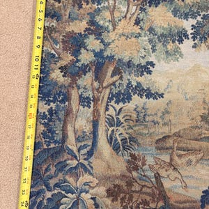 May include: A tapestry with a landscape scene featuring trees, water, and birds. The tapestry is primarily blue, beige, and brown. The length of the tapestry is approximately 27 inches.