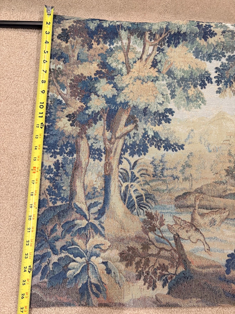 May include: A tapestry with a landscape scene featuring trees, water, and birds. The tapestry is primarily blue, beige, and brown. The length of the tapestry is approximately 27 inches.