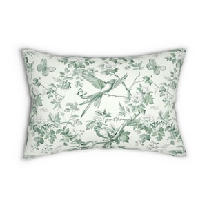 May include: A white pillow with a green floral pattern featuring birds and butterflies. The pattern is a repeating design of branches, leaves, flowers, and birds.
