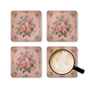 May include: A set of four square coasters featuring a pink background with a central bouquet of pink roses and green leaves, framed by an ornate beige border. One coaster supports a black mug filled with coffee featuring white latte art.