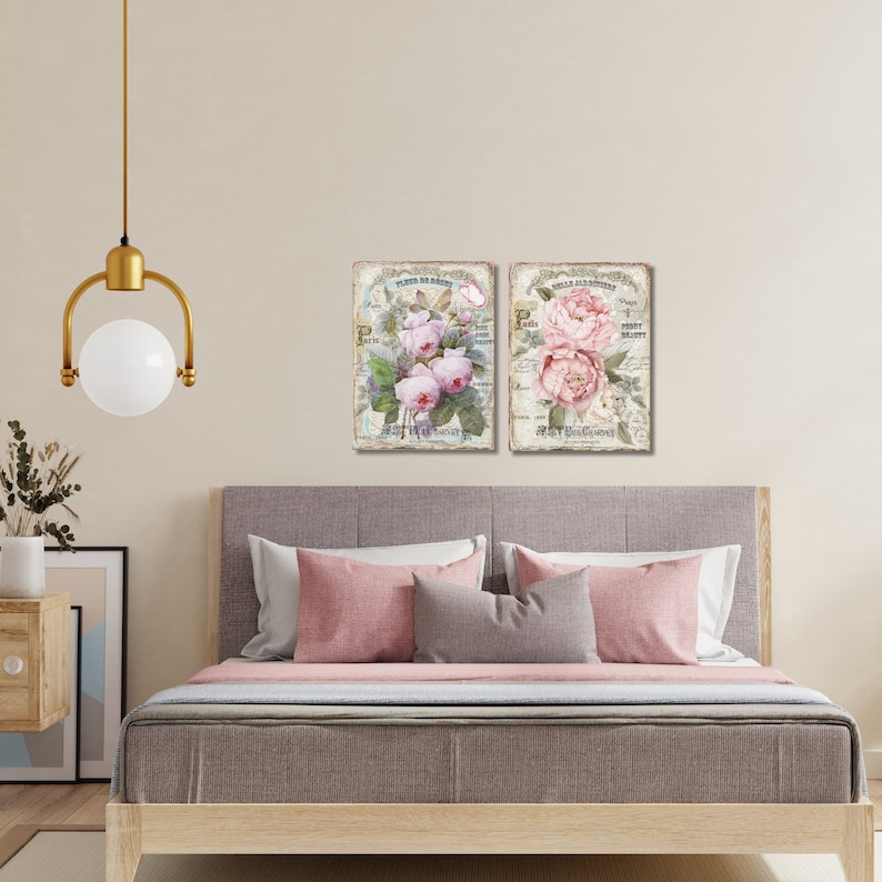 Op de afbeelding: Twee ingelijste bloemenprints met roze rozen en groene bladeren op een witte achtergrond. De prints bevatten Franse tekst en worden boven een bed met roze en grijze kussens weergegeven.