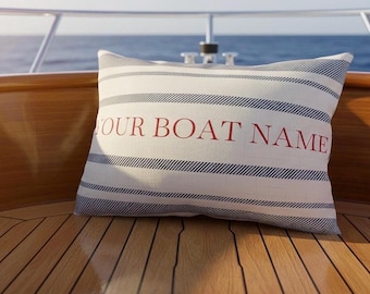 Könnte beinhalten: Ein rechteckiges Zierkissen mit weißem Hintergrund, horizontalen dunkelblauen Streifen und dem Text YOUR BOAT NAME in roten Buchstaben in der Mitte. Das Kissen liegt auf einer Oberfläche aus Holz.