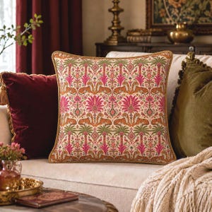 May include: A square throw pillow featuring a repeating pattern of orange tigers, green palm trees, and vibrant pink floral motifs on a cream background, finished with a thick gold twisted cord trim along all four edges of the cushion.