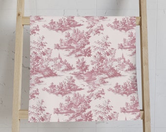 May include: A rectangular towel featuring a repeating toile de jouy pattern in a deep rose pink color against a pale blush pink background. The intricate design depicts pastoral landscapes with small houses, trees, and rolling hills throughout.