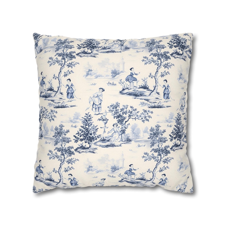 May include: A square throw pillow featuring a cream-colored background with a repeating blue toile de jouy pattern. The design depicts various figures in period clothing, trees, and landscape elements distributed across the fabric surface.