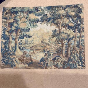 May include: A tapestry depicting a serene forest scene with trees, a river, and a distant landscape. The artwork features a color palette of blues, greens, and browns, creating a tranquil and naturalistic aesthetic. A heron stands near the water.