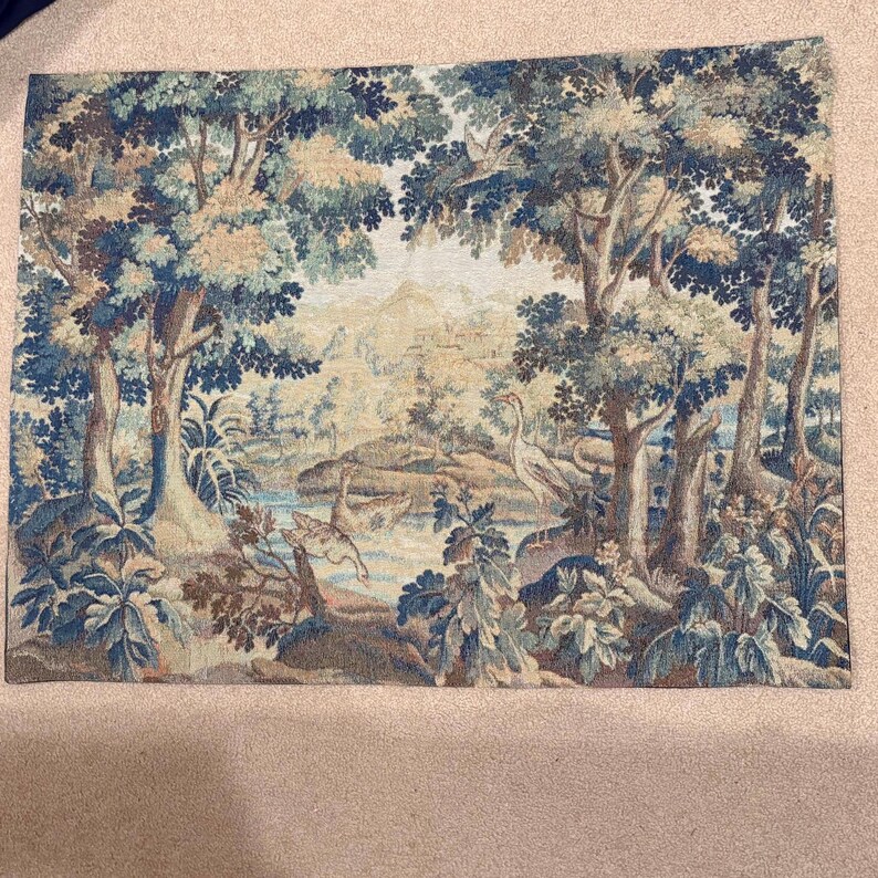 May include: A tapestry depicting a serene forest scene with trees, a river, and a distant landscape. The artwork features a color palette of blues, greens, and browns, creating a tranquil and naturalistic aesthetic. A heron stands near the water.