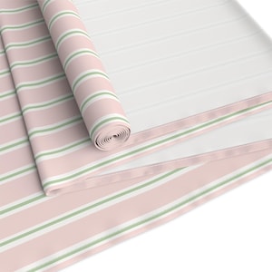 May include: A rolled-up fabric with a pink and white striped pattern, accented by thin green stripes. The fabric is partially unrolled, revealing a larger section with the same design. The overall aesthetic is soft and inviting, suitable for home decor.