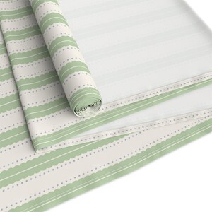 May include: A roll of fabric featuring a light cream background with repeating horizontal patterns. The design includes sage green scalloped bands alternating with thin sage green lines and rows of small, evenly spaced light blue dots.