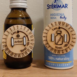 May include: Two bottles, one amber glass and one white spray bottle, each with a wooden timer. The amber bottle has "Arthur" on its timer. The spray bottle is labeled "ST&Eacute;RIMAR HIGIENA NOSA baby" and has "Margare" on its timer.