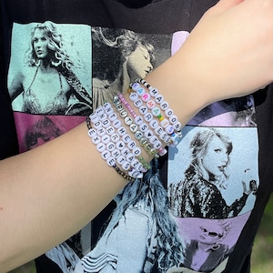 May include: A set of colorful beaded bracelets with words like "Maroon 5", "Fearless", "1989", "Reputation", "Lover", "Speak Now", "Red", "Taylor Swift", "Anti-Hero", "Midnights", "Enchanted", "Don't  You  Hate  When", "Exile", "Lights", "You  All  Over  Me", "The  Hero", "Wonderland", "End  Game", "You  Need  To  Calm  Down", "Delicate", "ME!" and "Look  What  You  Made  Me  Do" on them.