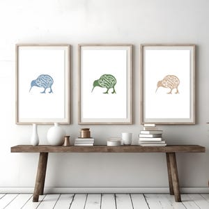 Puede incluir: Tres impresiones enmarcadas de un kiwi estilizado en azul, verde y marrón. Las impresiones están colgadas en una pared blanca sobre una mesa consola de madera con un jarrón de hierba de la pampa seca.