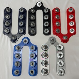 May include: A selection of U-shaped components made from metal and plastic, each with several ball bearings. The items are in different colours: blue, black, red, and silver. The bearings are silver and the objects are on a white surface.