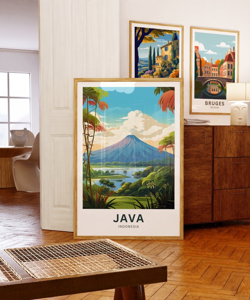 May include: Three framed art prints. The largest features a landscape of Java, Indonesia, with a volcano, lush greenery, and the text "JAVA INDONESIA." Other prints depict European scenes. All are in wooden frames, displayed on a wooden cabinet.