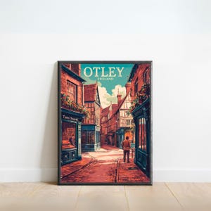 Puede incluir: Una impresión artística enmarcada de Otley, Inglaterra, con una ilustración al estilo acuarela de una escena callejera. La obra de arte muestra edificios con fachadas de ladrillo rojo, escaparates y una persona caminando por la calle adoquinada. La impresión incluye el texto "OTLEY ENGLAND".