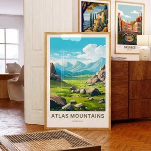 Op de afbeelding: Drie ingelijste kunstdrukken. De grootste toont een landschap van het Atlasgebergte in Marokko, met de tekst "ATLAS MOUNTAINS MOROCCO". Twee kleinere prenten tonen Europese stadsgezichten. Allemaal tentoongesteld op een houten vloer.