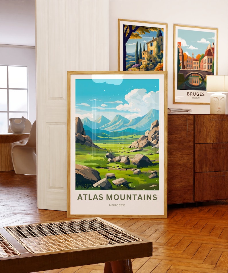 Op de afbeelding: Drie ingelijste kunstdrukken. De grootste toont een landschap van het Atlasgebergte in Marokko, met de tekst "ATLAS MOUNTAINS MOROCCO". Twee kleinere prenten tonen Europese stadsgezichten. Allemaal tentoongesteld op een houten vloer.