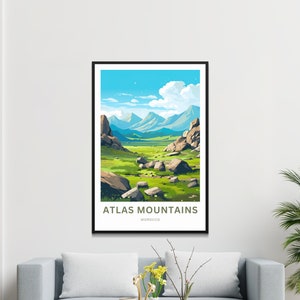 Op de afbeelding: Een ingelijste kunstdruk met een gestileerd landschap van het Atlasgebergte in Marokko. Het kunstwerk toont een groene vallei met grote rotsen, onder een blauwe lucht met witte wolken. De tekst "ATLAS MOUNTAINS MOROCCO" staat onderaan.