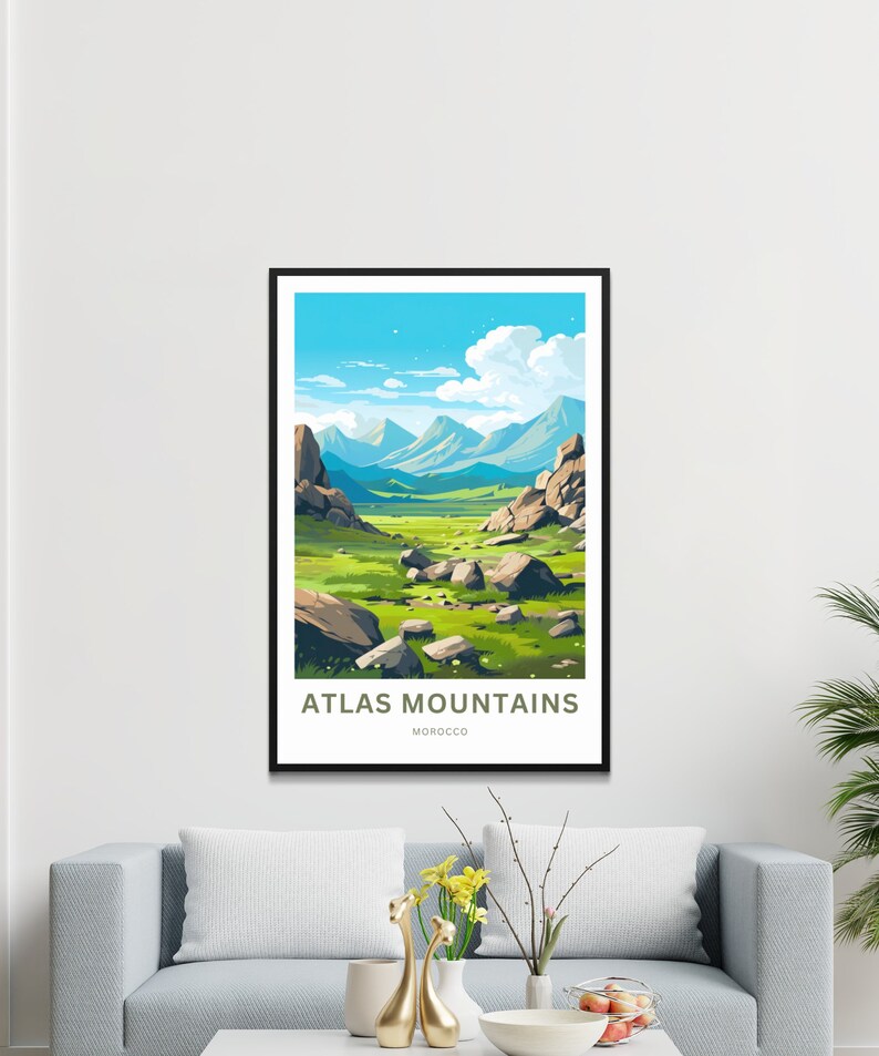 Op de afbeelding: Een ingelijste kunstdruk met een gestileerd landschap van het Atlasgebergte in Marokko. Het kunstwerk toont een groene vallei met grote rotsen, onder een blauwe lucht met witte wolken. De tekst "ATLAS MOUNTAINS MOROCCO" staat onderaan.