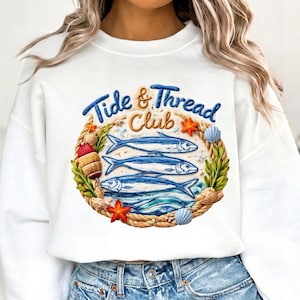 May include: White sweatshirt featuring a nautical design. The design includes the text "Tide & Thread Club" in blue, a rope circle, three blue fish, starfish, seashells, and greenery. A stylish and comfortable garment.