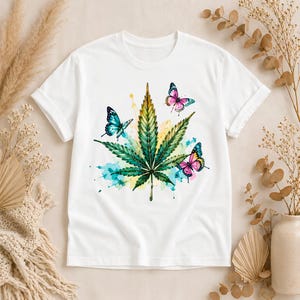 Peut inclure: Un t-shirt blanc &agrave; manches courtes arborant un motif central compos&eacute; d'une feuille de cannabis verte entour&eacute;e d'&eacute;claboussures d'aquarelle jaune, bleue et turquoise, agr&eacute;ment&eacute; de trois papillons color&eacute;s aux tons bleu, rose et violet.