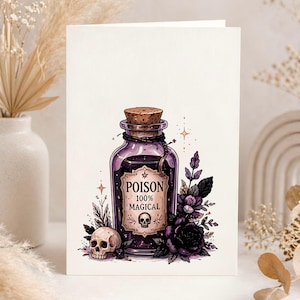May include: A greeting card featuring a purple potion bottle with a cork stopper, labeled "POISON 100% MAGICAL" with a skull graphic. The card is decorated with black roses, leaves, and a small skull.