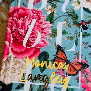 May include: A blue journal with a floral design and gold lettering. The text on the cover reads "Bible" and "Monica Langlie".