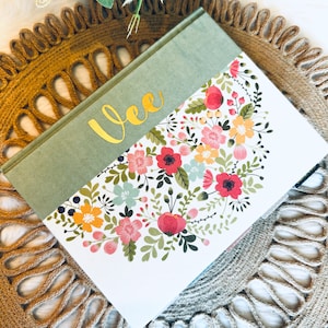 May include: A green and white journal with a floral design and the name "Vee" in gold lettering.