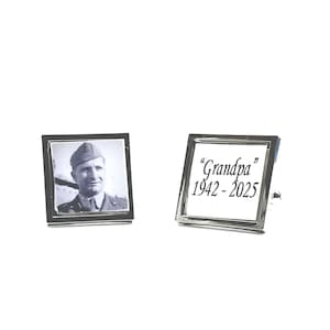 May include: A pair of silver cufflinks. One cufflink features a black and white photo of a man in uniform. The other cufflink has the text "Grandpa" and the years "1942-2025" in black script.