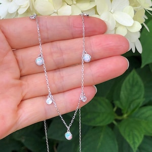 May include: A silver chain necklace with multiple small opal and clear gemstone pendants. The necklace is layered and has a delicate design.