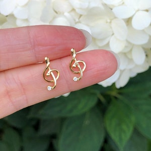 May include: A pair of gold-tone earrings shaped like treble clefs with a small clear rhinestone in the center of each clef.