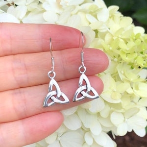 May include: Silver Celtic knot earrings with a triangular shape. The earrings are hanging from a person's hand.