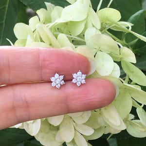 May include: A pair of silver flower-shaped earrings with small white diamonds.