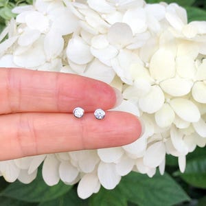 May include: A pair of small, round, silver stud earrings with clear, sparkling stones.