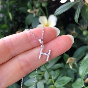 May include: A silver chain necklace with a pendant in the shape of the letter H. The pendant is encrusted with small, clear gemstones.