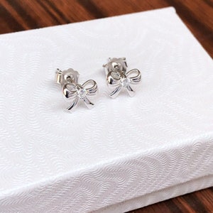 May include: A pair of silver bow-shaped earrings with a small clear rhinestone in the center of each bow.