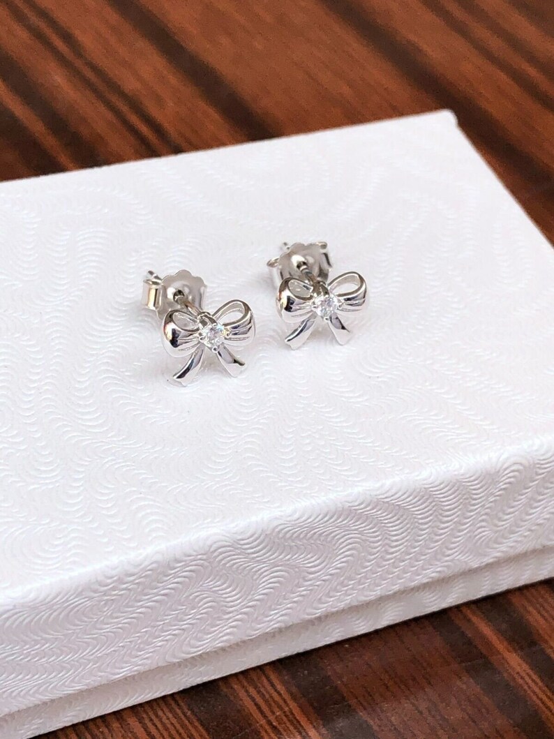 May include: A pair of silver bow-shaped earrings with a small clear rhinestone in the center of each bow.
