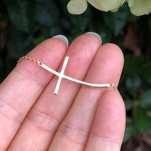 May include: A gold-toned necklace with a curved cross pendant. The necklace is delicate and features a simple chain.