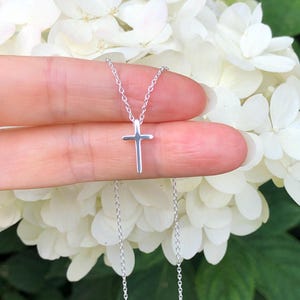 May include: A delicate silver chain necklace with a small, simple cross pendant.