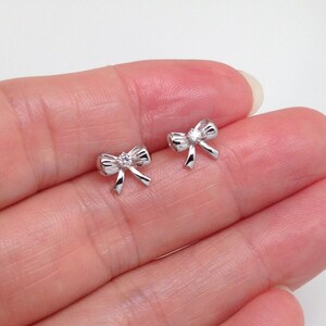 May include: A pair of silver bow earrings with a small clear rhinestone in the center of each bow.