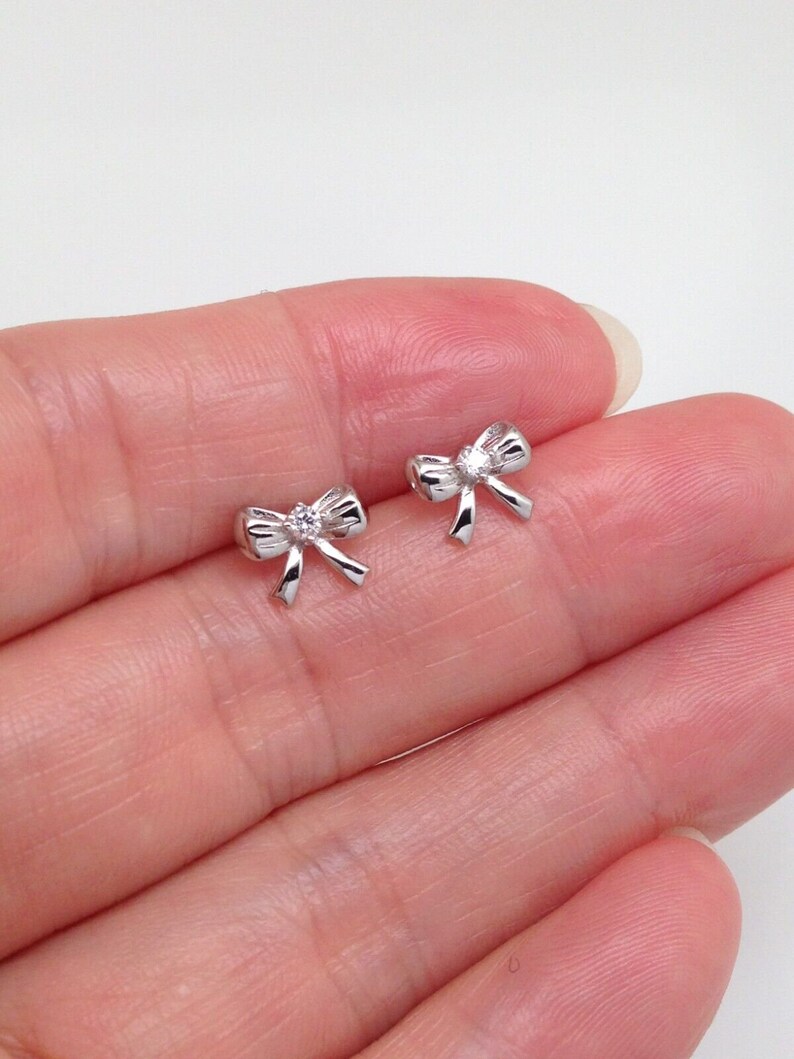 May include: A pair of silver bow earrings with a small clear rhinestone in the center of each bow.