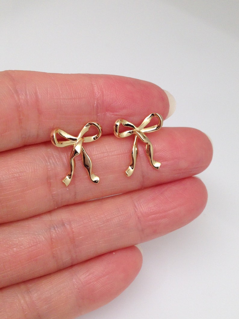 Puede incluir: Un par de pendientes de bot&oacute;n de oro en forma de lazo. Los pendientes son peque&ntilde;os y delicados, y ser&iacute;an un gran regalo para una ocasi&oacute;n especial.