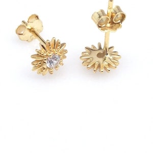 Peut inclure: Une paire de boucles d'oreilles &agrave; clous dor&eacute;es. Chaque boucle d'oreille pr&eacute;sente un motif floral avec une pierre pr&eacute;cieuse claire au centre. Les p&eacute;tales de la fleur sont d&eacute;taill&eacute;s, et les boucles d'oreilles ont des fermoirs &agrave; poussette. Les boucles d'oreilles sont sur fond blanc.