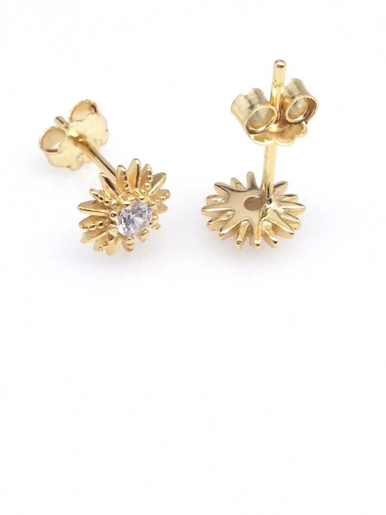 Peut inclure: Une paire de boucles d'oreilles &agrave; clous dor&eacute;es. Chaque boucle d'oreille pr&eacute;sente un motif floral avec une pierre pr&eacute;cieuse claire au centre. Les p&eacute;tales de la fleur sont d&eacute;taill&eacute;s, et les boucles d'oreilles ont des fermoirs &agrave; poussette. Les boucles d'oreilles sont sur fond blanc.