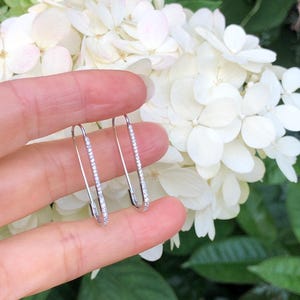 May include: A pair of silver safety pin earrings with a row of small clear cubic zirconia stones on each pin.