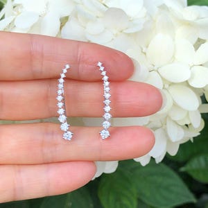 May include: A pair of silver ear climbers with a row of small, clear cubic zirconia stones.
